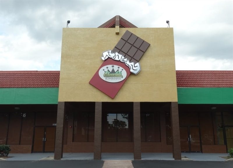 '초콜릿 왕국' 을 읽으며 부분적으로 초콜릿 바를 포장하지 않은 커다란 간판이 있는 건물 외관. 벽돌 기둥과 흐린 하늘.