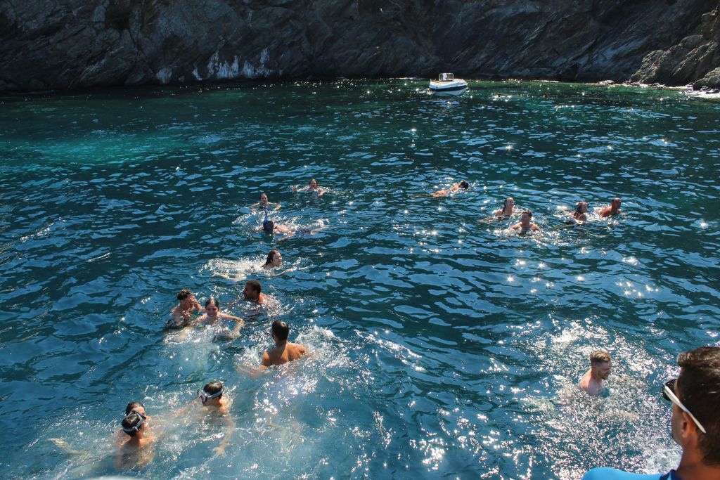 바위 해안 근처의 맑고 푸른 물에서 수영하는 사람들로, 근처에 작은 보트가 떠 있습니다.