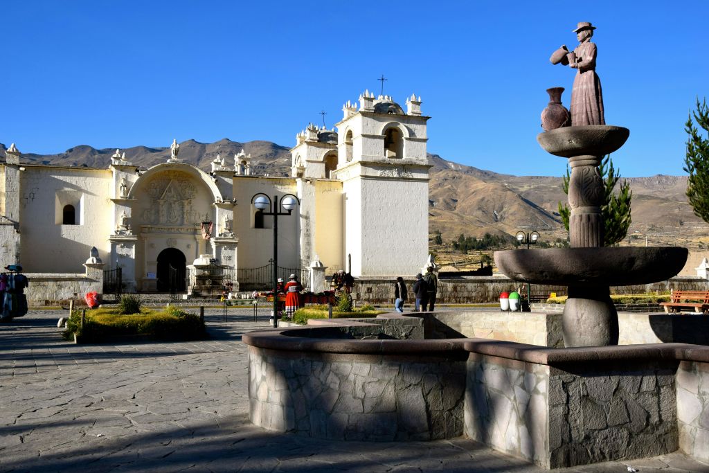 광장에 종탑이 있는 하얀 교회, 뒷산, 산책하는 사람들, 전경에 있는 석조 분수.