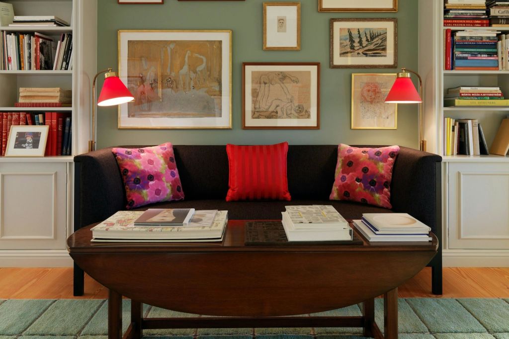 검은색 소파가 놓인 거실, 빨간색과 꽃무늬 쿠션, 책이 놓인 나무 커피 테이블, 초록색 벽에 액자 모양의 예술품이 놓여 있습니다.