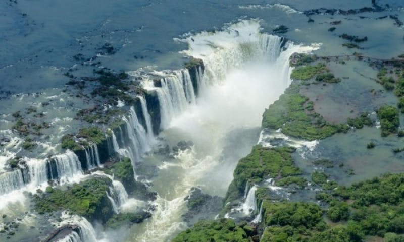 울창한 녹지와 바위 지형으로 둘러싸인 강으로 이어지는 여러 개의 강이 흐르는 강력한 폭포의 공중 전망.