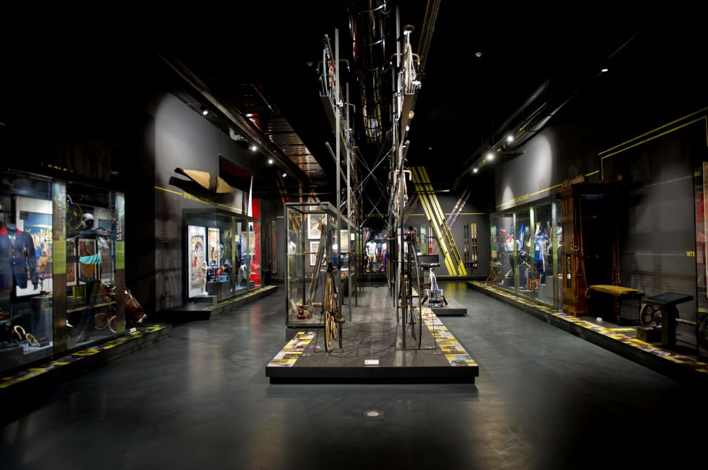 중앙 금속 조각이 있는 유리 케이스의 다양한 디스플레이와 유물을 전시하는 희미한 조명의 박물관 갤러리입니다.