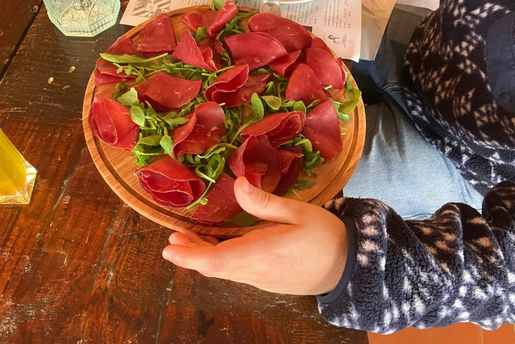 나무 테이블에 잘게 썬 고기와 신선한 채소가 담긴 나무 접시를 들고 있는 사람.