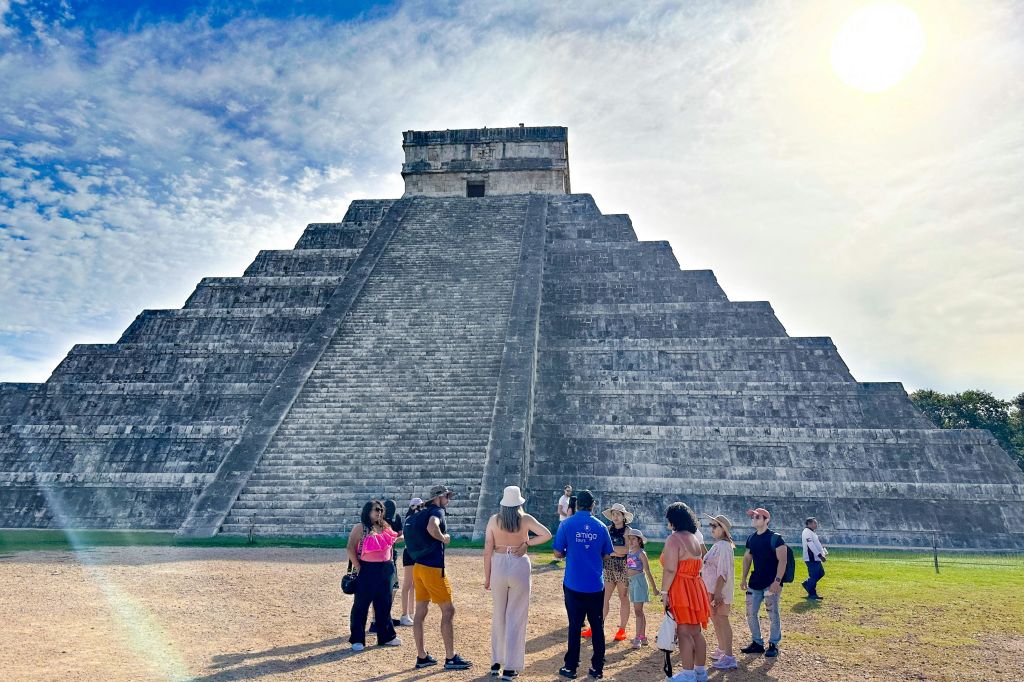 한 무리의 사람들이 부분적으로 흐린 하늘 아래 크고 오래된 피라미드 앞에 서 있습니다.
