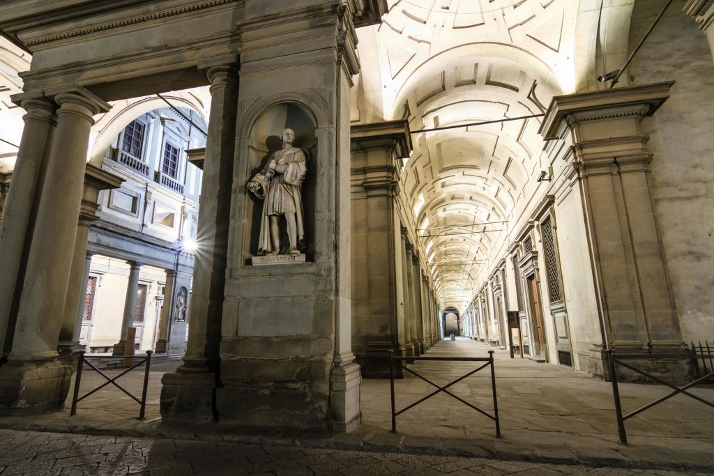 아치형 천장과 기둥, 전경의 받침대에 있는 한 남자의 동상이 있는 웅장한 건축물 복도입니다.