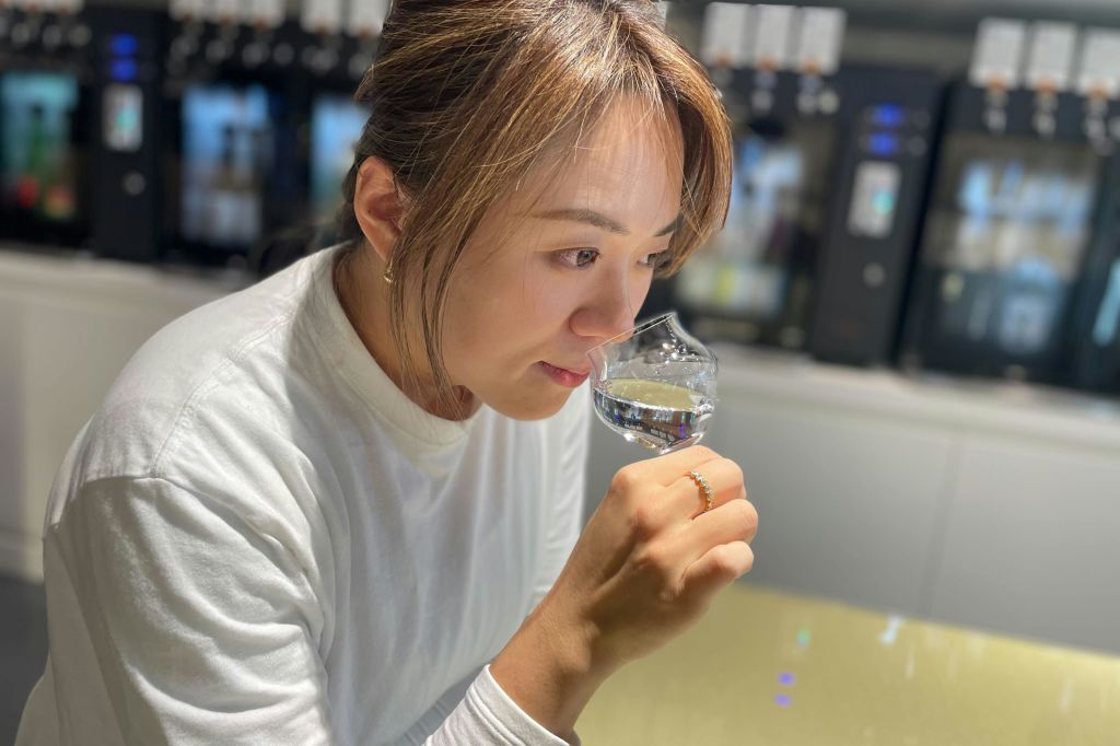 흰색 셔츠를 입은 사람이 현대적인 실내 환경에서 투명한 액체 잔을 냄새 맡고 있습니다.