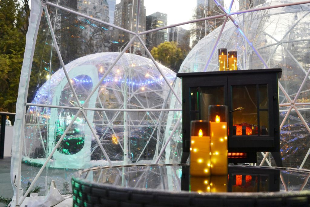 근처 테이블에 요정 조명과 빛나는 촛불이 있는 지오데식 돔. 야외에 보이는 도시 풍경과 나무.