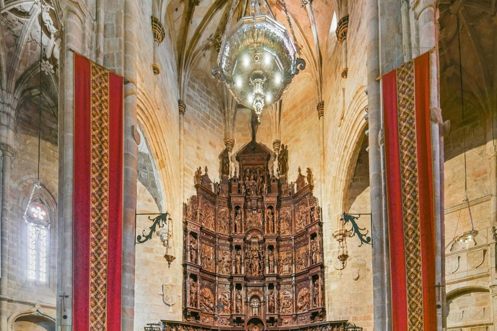 높은 석조 아치와 커다란 샹들리에가 있는 대성당 내부에 정교한 조각이 있는 화려한 나무 제단.