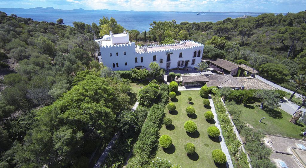 바다 근처에 울창한 녹지로 둘러싸인 잘 손질된 정원이 있는 하얀 성 모양의 건물의 공중 전망.