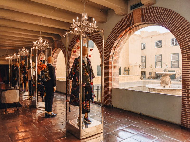 분수가 있는 안뜰이 내려다보이는 아치형 창문 근처의 샹들리에 아래 꽃무늬 의상을 입은 마네킹.