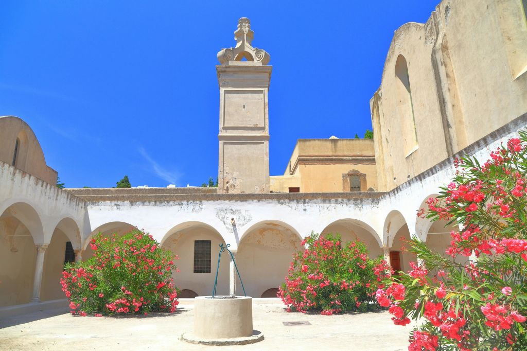 맑고 푸른 하늘 아래 아치형 통로와 꽃이 만발한 수풀로 둘러싸인 중앙 우물이 있는 안뜰.