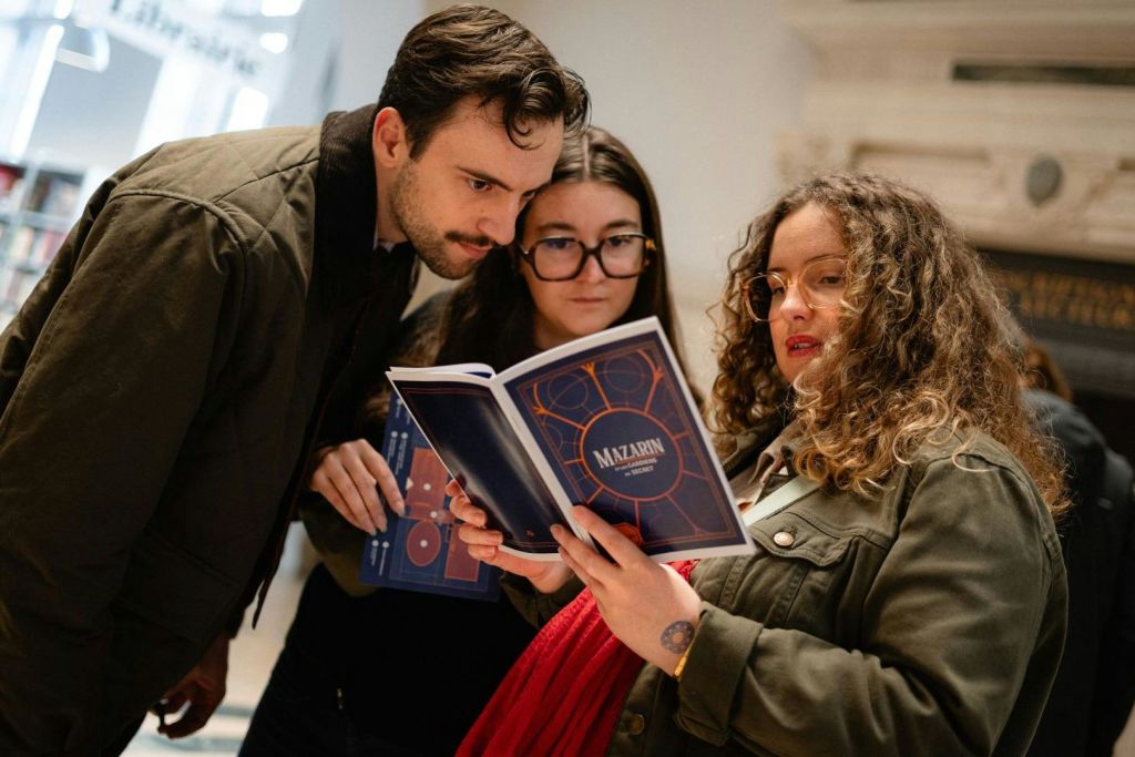 세 사람이 'Mazarin' 이라는 열린 소책자를 보고 있습니다. 그들은 그것에 대해 면밀히 논의하거나 검토하고 있는 것 같습니다.