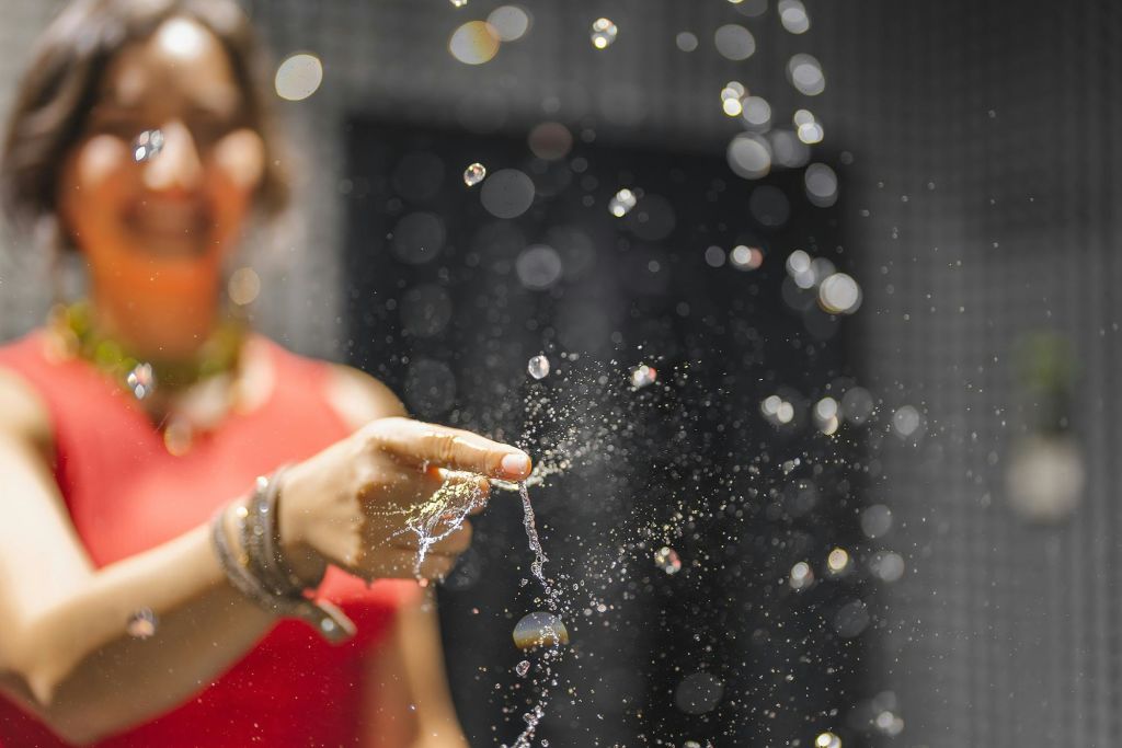 빨간 상단에 있는 사람이 물줄기에 닿아 흐릿한 어두운 배경에 반짝이는 물방울을 만듭니다.