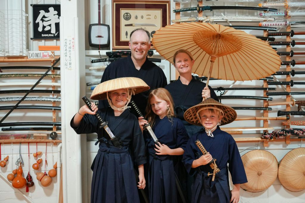 일본 전통 의상을 입은 한 가족이 칼과 우산을 들고 칼 앞에 서 있습니다.