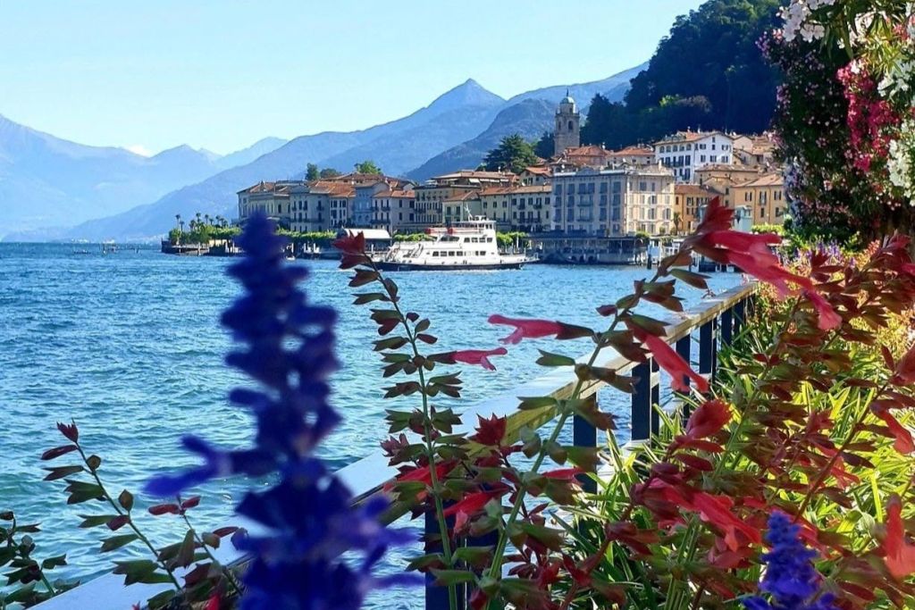 맑고 푸른 하늘 아래 산으로 둘러싸인 배가 정박한 호숫가 마을의 풍경을 형형색색의 꽃으로 장식합니다.