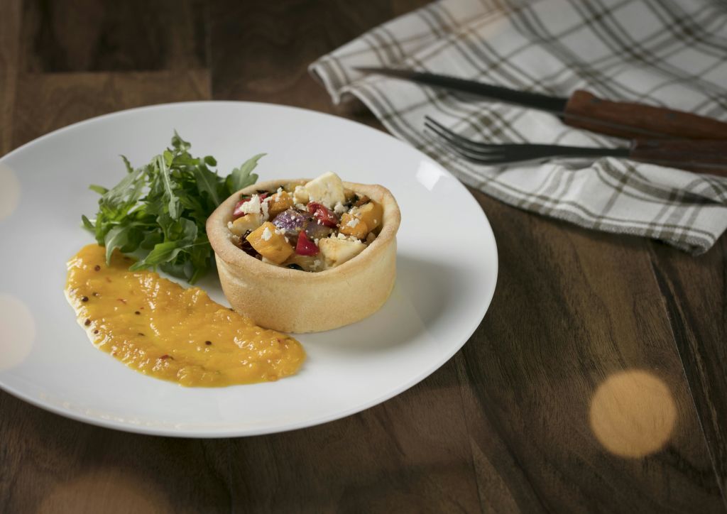 야채와 노란 소스를 곁들인 혼합 충전재가 들어간 작은 페이스트리로, 냅킨과 식기 옆에 흰색 접시에 놓습니다.