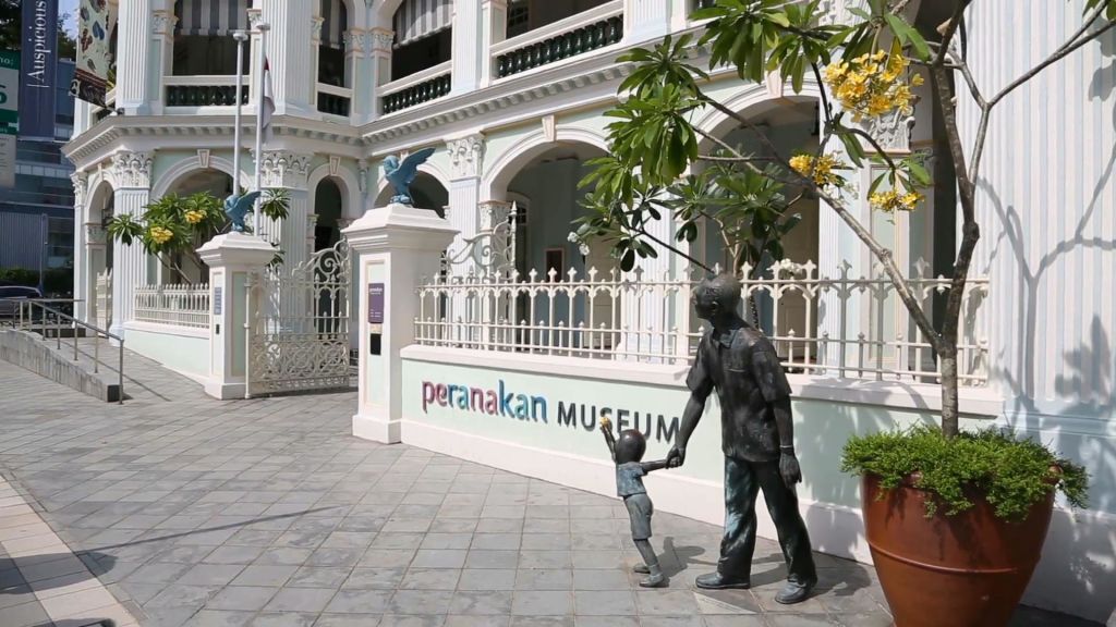 출입문 근처에서 손을 잡고 있는 남성과 어린이의 동상이 있는 페라나칸 박물관 외관.