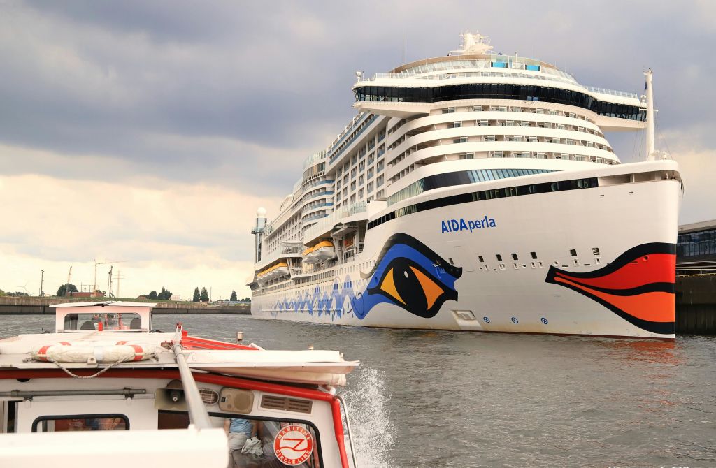 흐린 날 작은 모터보트 옆의 강에서 항해하는 "AIDAperla" 라는 이름의 대형 유람선.