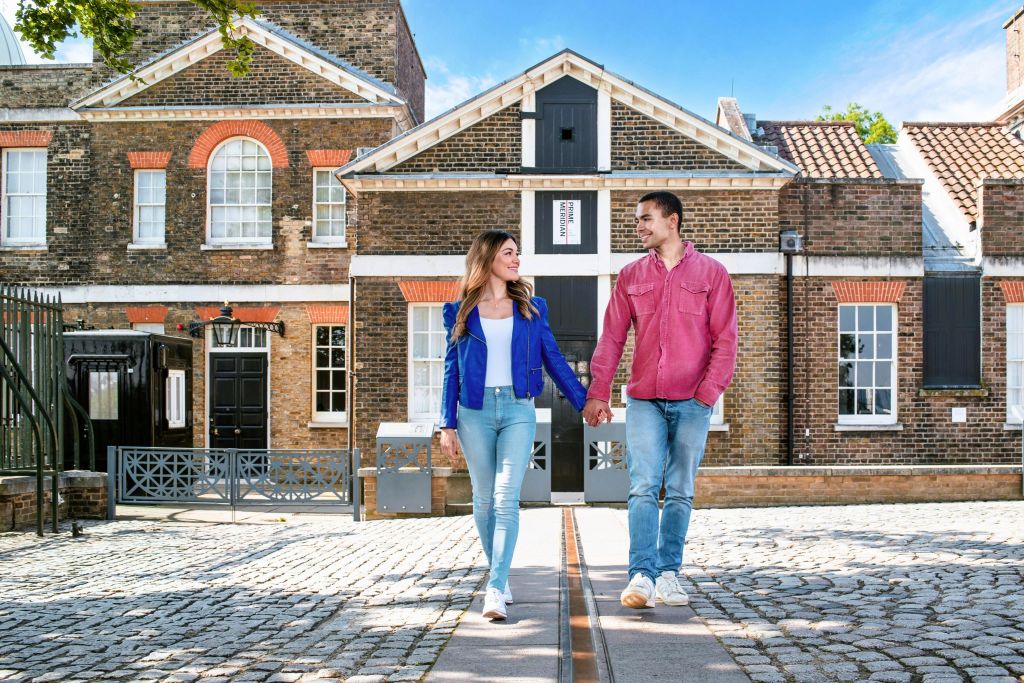 맑고 푸른 하늘 아래 유서 깊은 벽돌 건물 앞 자갈길을 걷던 커플이 손을 잡고 있습니다.