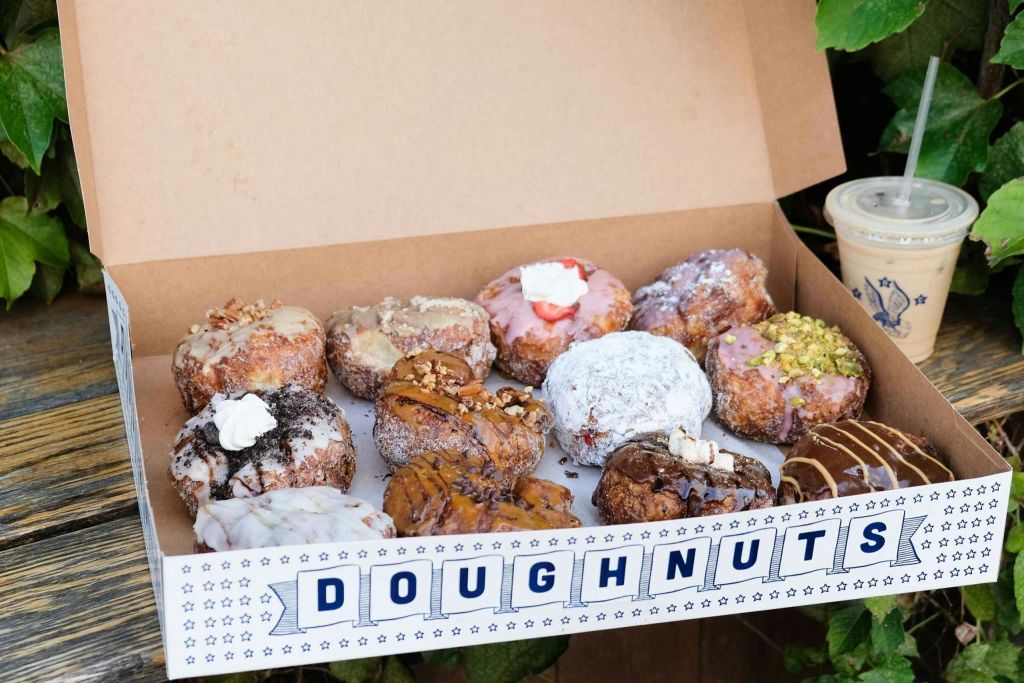 '도넛' 이라고 표시된 크림, 견과류, 설탕 가루 등 다양한 토핑이 토핑된 모듬 도넛 상자.