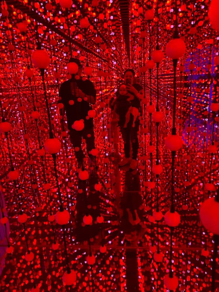 수많은 빨간색과 주황색 LED 조명이 비춰진 미러룸에 한 가족이 서서 무한한 반사 효과를 냅니다.