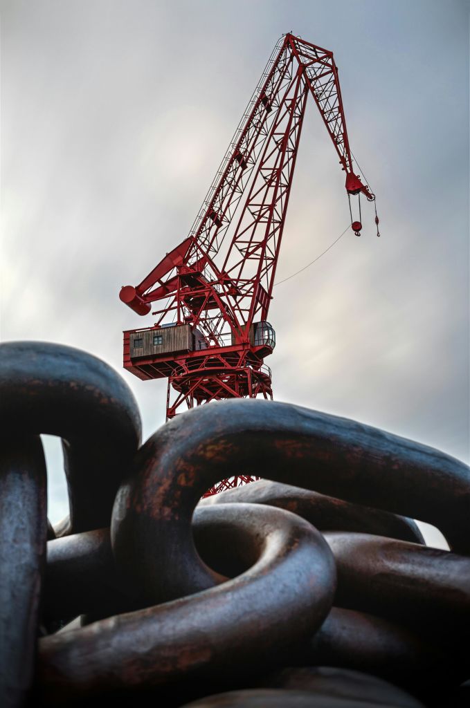 흐린 하늘 배경의 빨간색 산업용 크레인, 전경에 대형 금속 체인 링크.