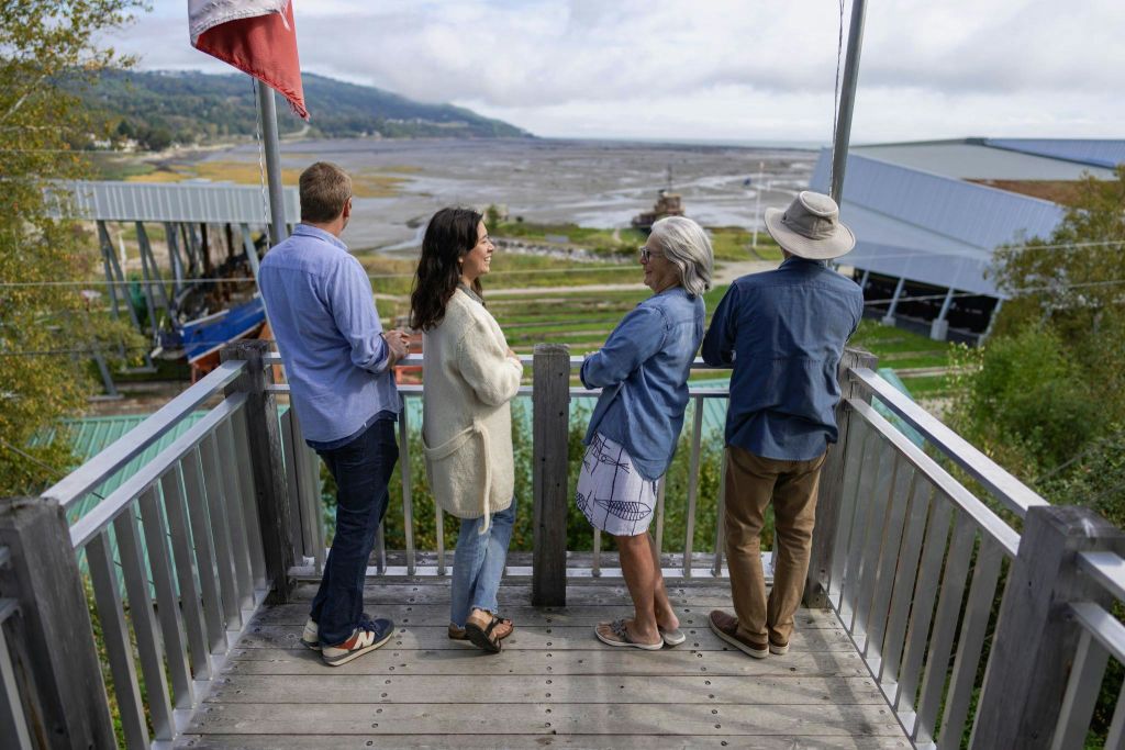 해안 경관이 내려다보이는 나무 데크에는 해안 평면, 보트, 먼 언덕 등 4명이 서 있습니다.