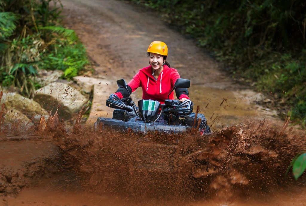 숲길의 흙탕물을 뚫고 ATV를 타고 빨간색 재킷과 노란색 헬멧을 착용한 사람.