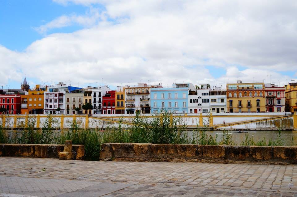 탁한 하늘 아래 다채로운 건물이 줄지어 있고, 앞쪽에는 돌담과 잔디가 있습니다.