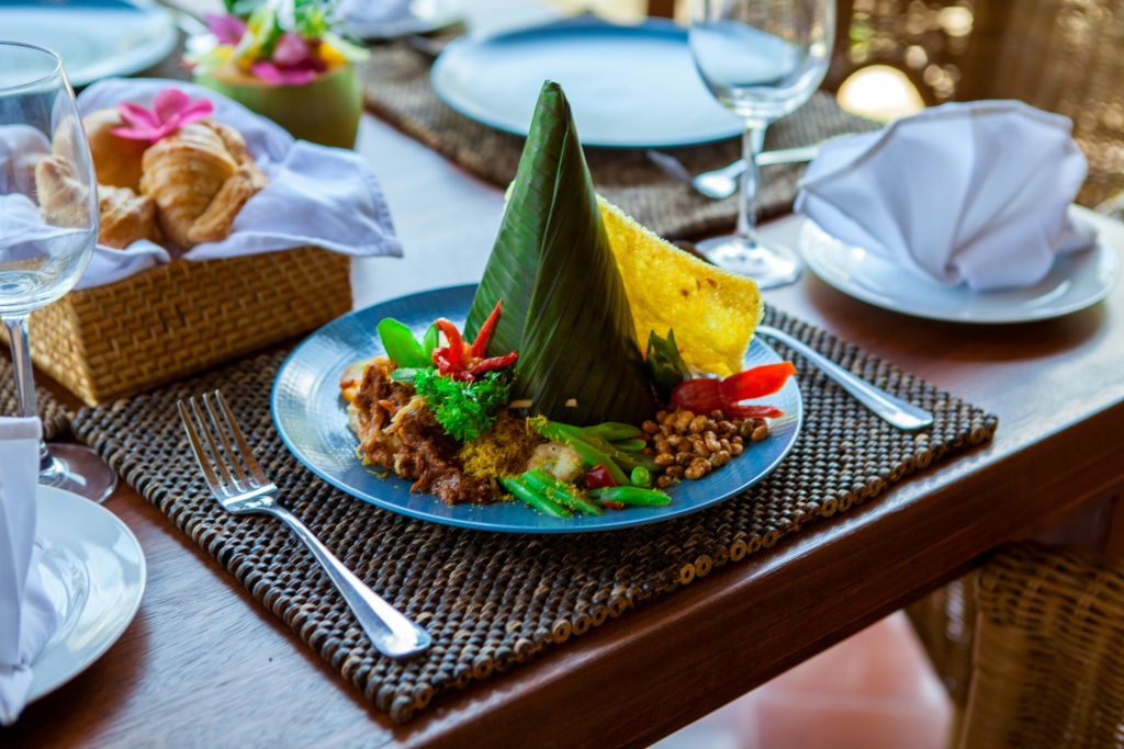 바나나 잎에 야채와 고기를 싸서 식기류와 함께 짠 플레이스매트 위에 올린 밥 한 접시.