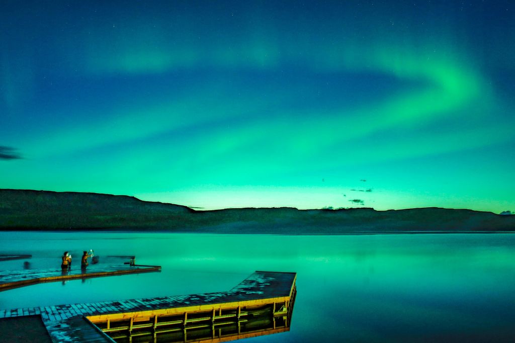 나무로 지어진 선착장은 활기찬 녹색과 파란색의 오로라 아래 잔잔한 호수로 뻗어 있습니다.