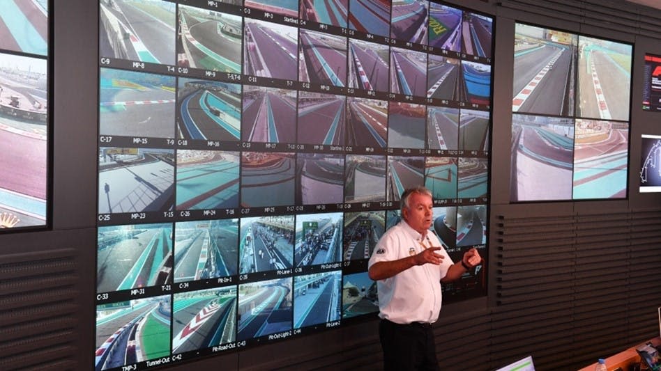 한 남성이 다양한 레이스 트랙 카메라 피드를 표시하는 커다란 모니터 벽 앞에 서 있습니다.