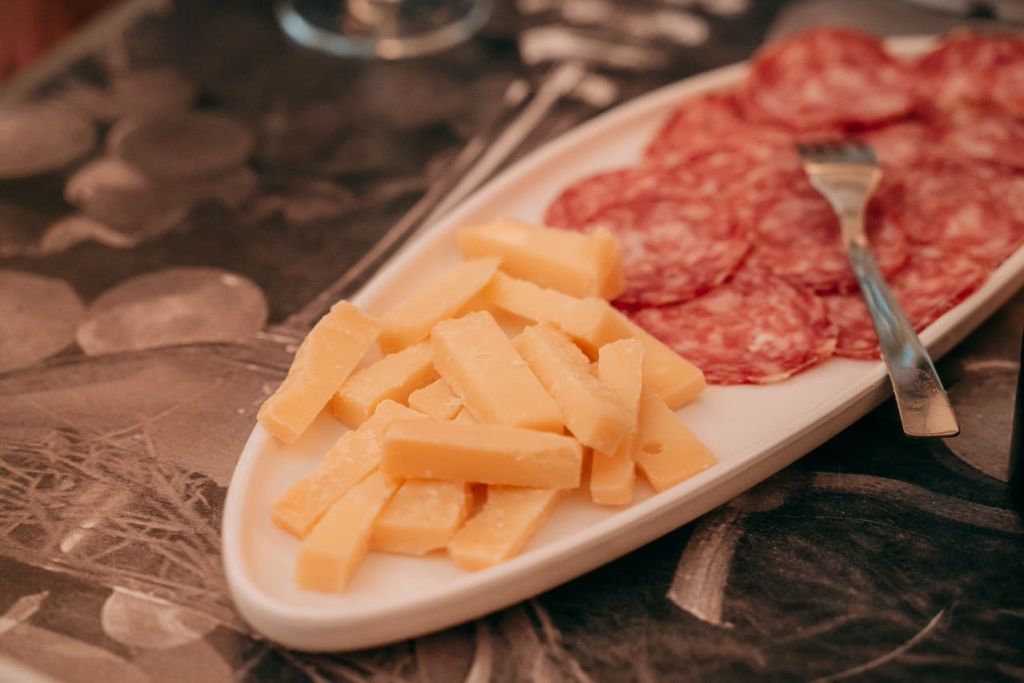 슬라이스 치즈와 살라미가 놓인 흰색 접시가 테이블 위에 놓여 있습니다.