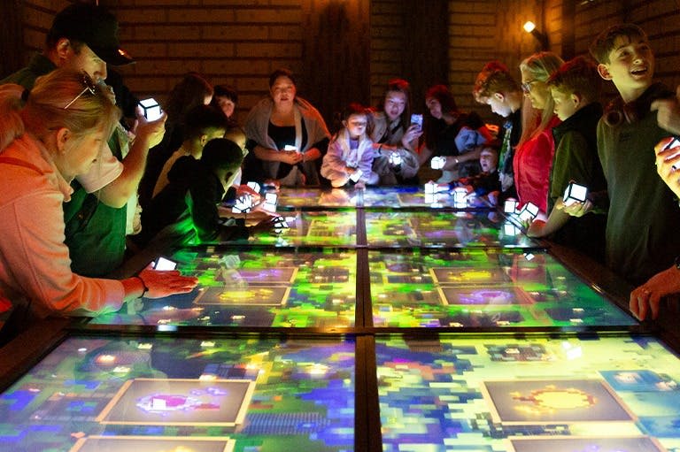 조명이 희미한 방에서 다채로운 그래픽을 보여주는 빛나는 대화형 테이블과 상호 작용하는 사람들.