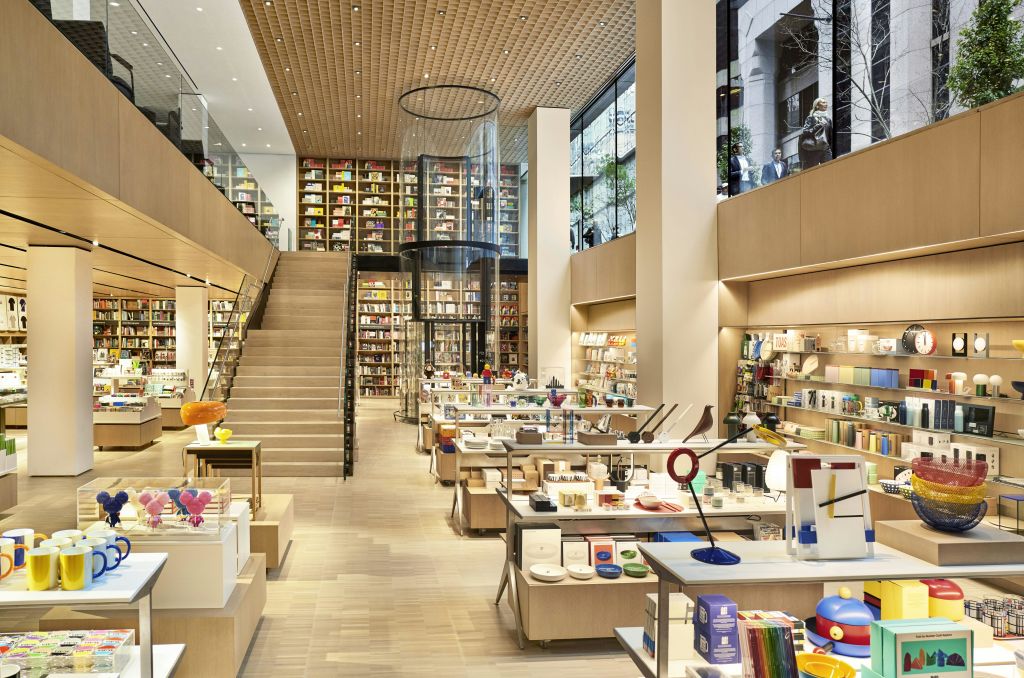 목재 선반, 다양한 상품, 중앙 계단, 대형 유리창이 있는 2층 현대식 서점.