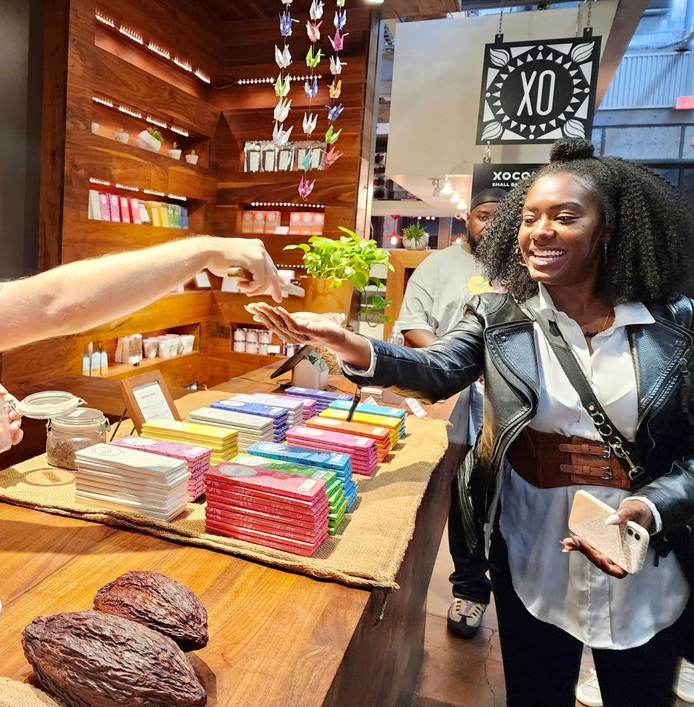 웃는 여성이 화려한 초콜릿 가게에서 납품업자로부터 코코아 팟이 전면에 표시된 물품을 받습니다.