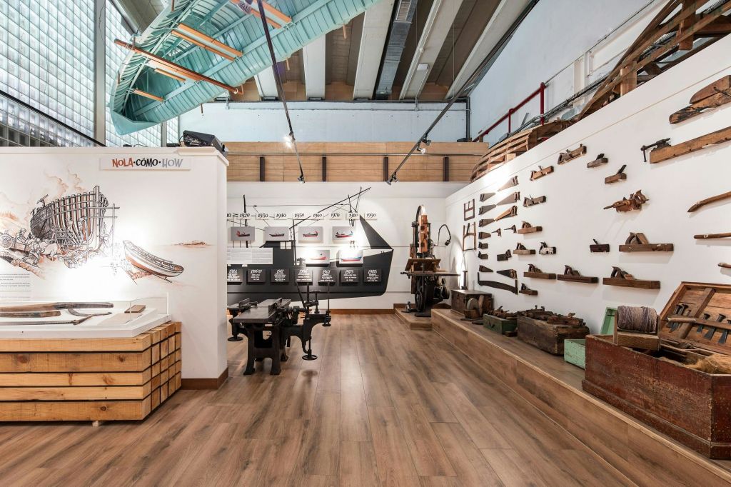 나무 바닥과 높고 탁 트인 천장이 있는 채광이 좋은 방에 벽과 테이블에 빈티지 목공 도구가 전시되어 있습니다.