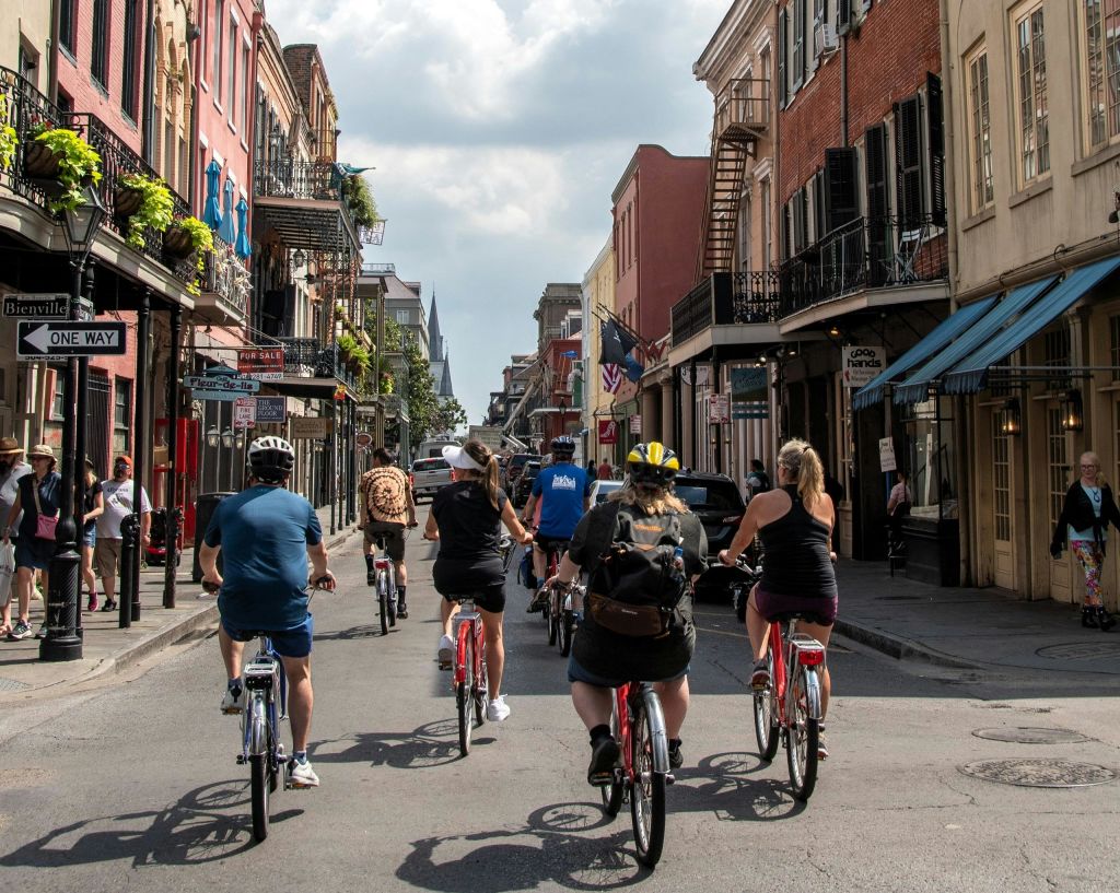 부분적으로 흐린 하늘 아래 화려한 건물과 상점이 늘어선 거리를 자전거로 달리는 사람들이 있습니다.