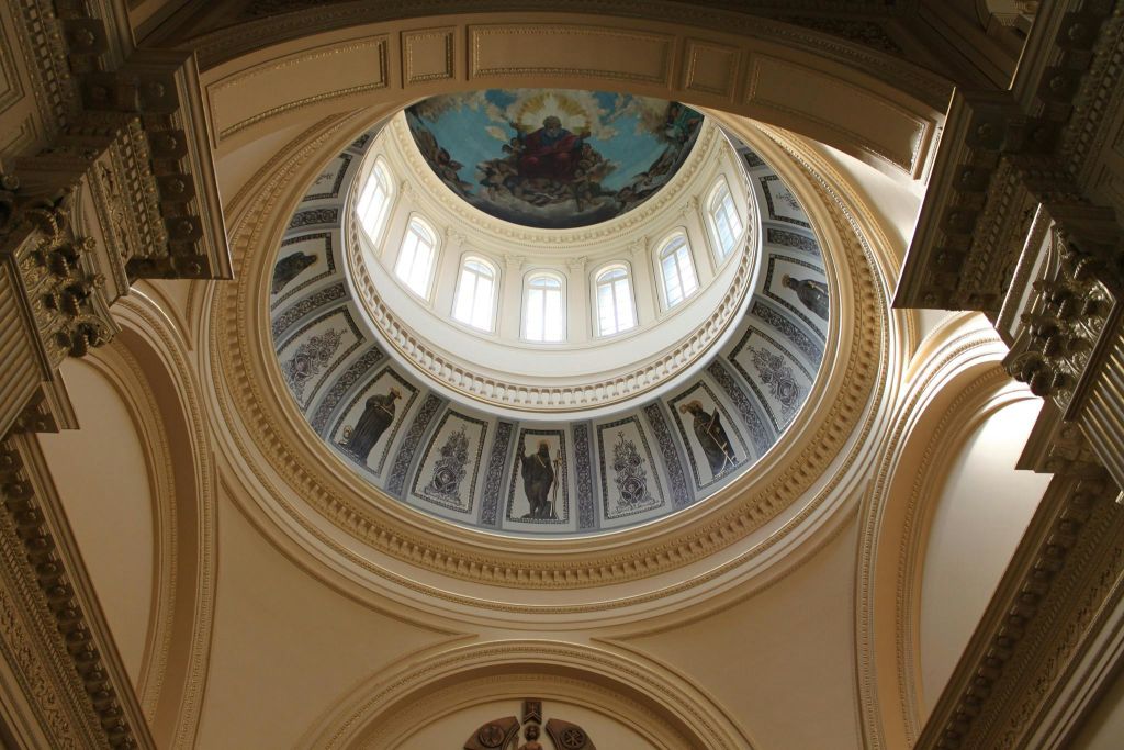 작은 아치형 창문으로 둘러싸인 디테일한 프레스코화로 장식된 화려한 돔 내부. 중앙 프레스코화는 천상의 장면을 묘사합니다.