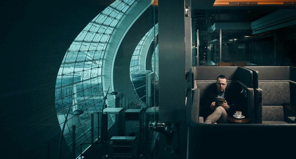 한 남성이 카페의 전용 부스에 앉아 태블릿을 읽고 있는데, 옆 테이블에 커피잔과 받침이 놓여 있습니다.