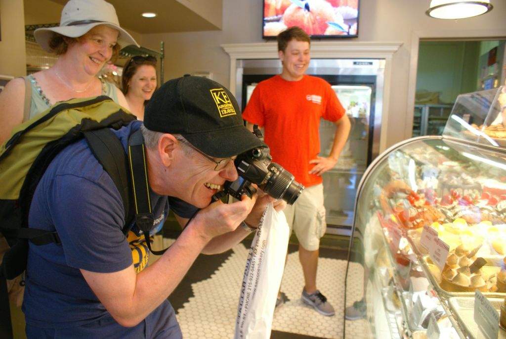 모자를 쓴 남자가 열정적으로 사진을 찍고 있고, 배경의 세 사람이 웃고 있습니다.