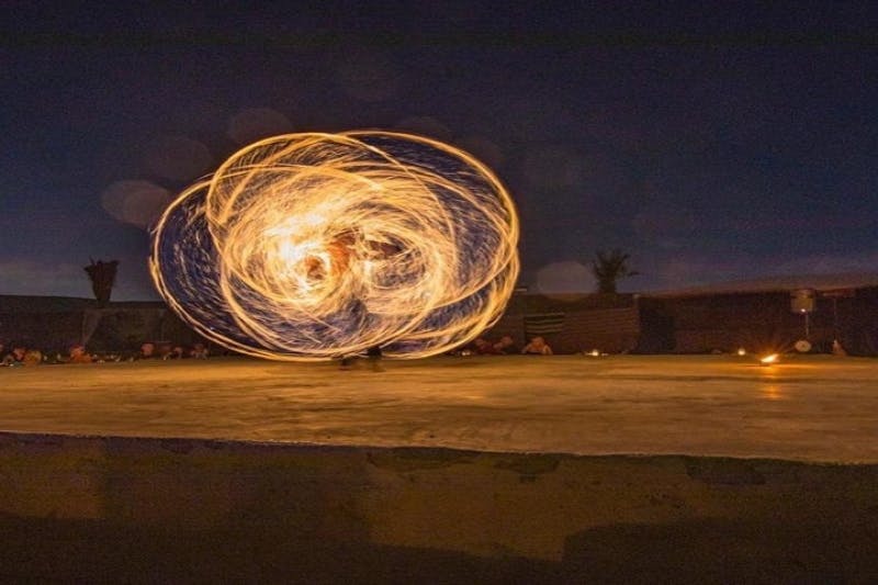 연기자가 여러 불 포이를 돌리며 어두운 야외 배경에 소용돌이치는 빛 패턴을 만듭니다.