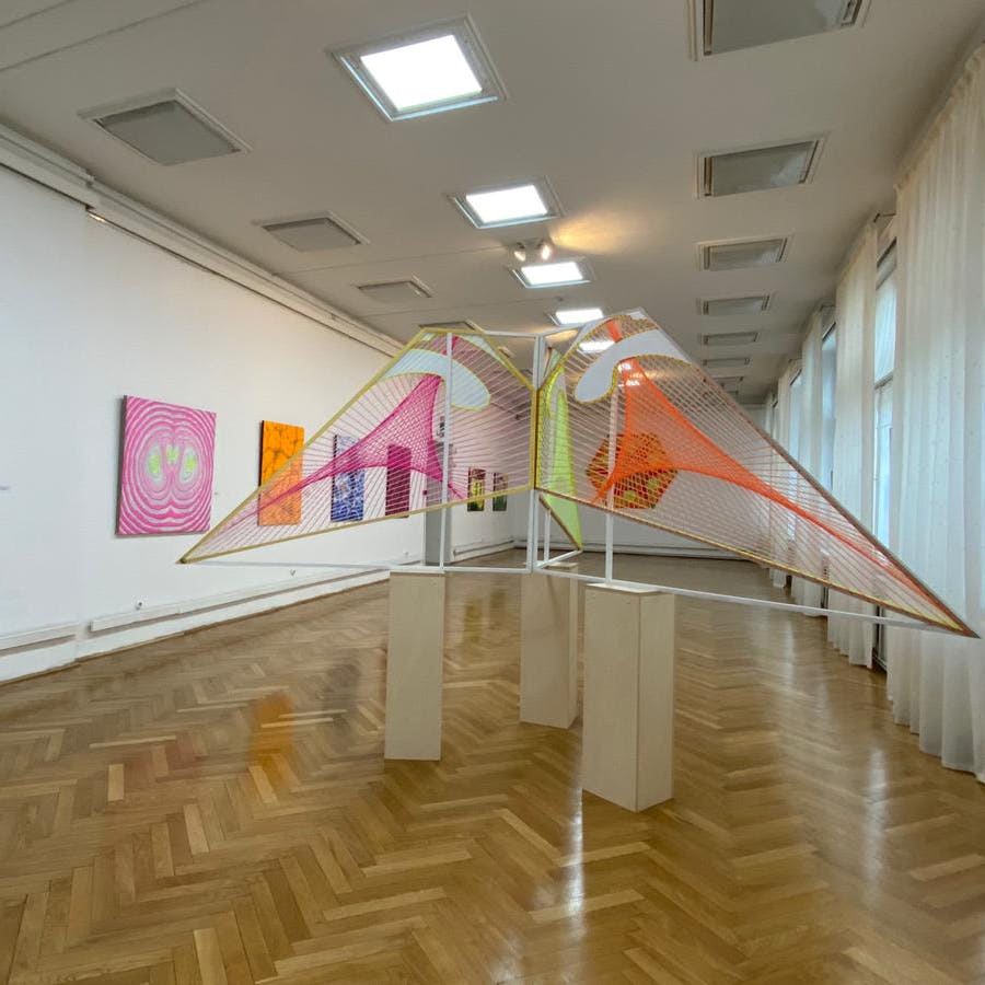 흰색 벽에 다채로운 기하학적 설치물과 추상적인 그림, 광택이 나는 나무 바닥이 있는 미술관.