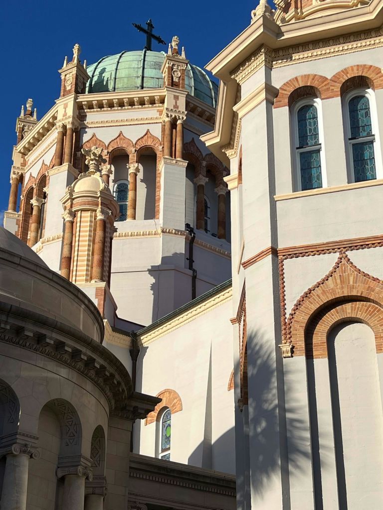 디테일한 아치와 기둥, 녹색 돔이 있는 화려한 건물로, 맑고 푸른 하늘 아래 정교한 건축 디자인이 돋보입니다.