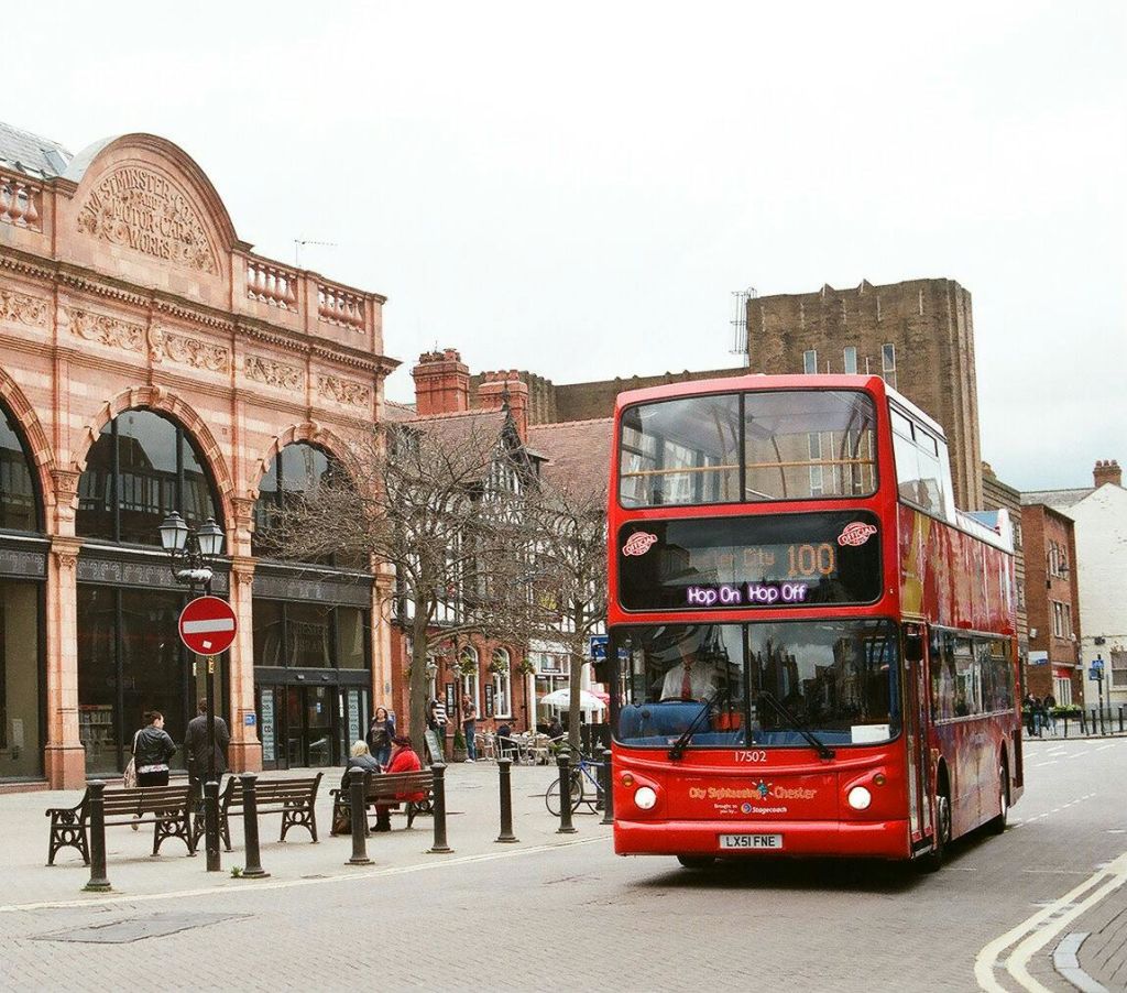 유서 깊은 건물과 보행자가 있는 거리에 빨간색 2층 버스가 '홉온홉오프 (Hop On Hop Off)' 라고 적혀 있습니다.