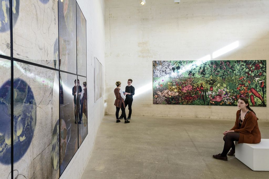 사람들은 현대적인 미니멀리즘 갤러리에서 다채로운 예술 작품을 감상합니다. 한 여성이 흰색 벤치에 앉아 있습니다.