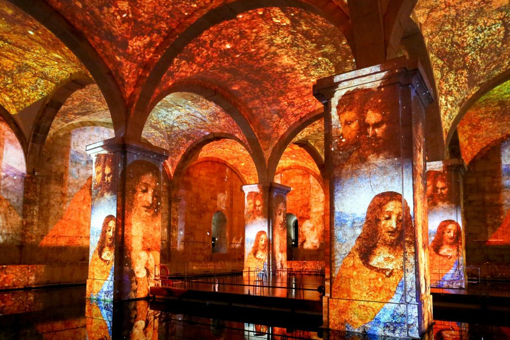 르네상스 예술 작품이 투영된 아치형 천장과 기둥이 있는 전시 공간입니다.