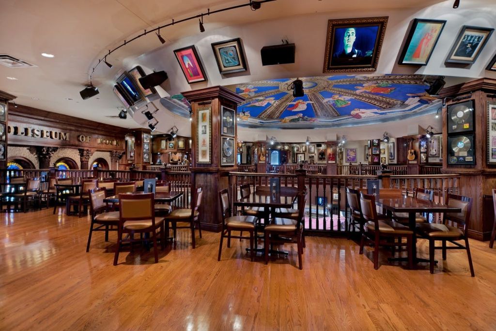 나무 바닥, 테이블, 의자가 있는 레스토랑 인테리어로 벽과 천장에 액자형 예술품이 있습니다.