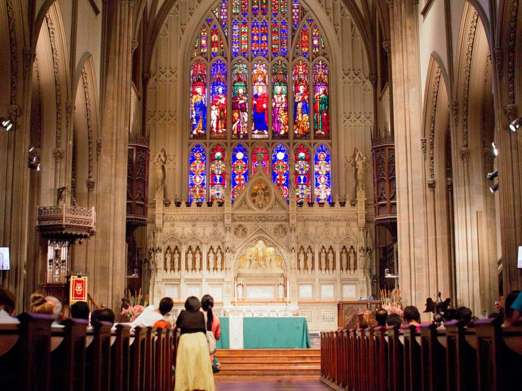 교회에 앉아 화려한 스테인드글라스 창문이 있는 화려한 제단을 마주하고 있는 사람들.