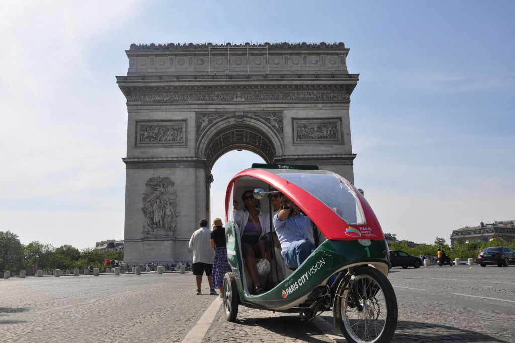 파리의 개선문 앞에서 승객을 태운 페디캡. 다른 보행자가 배경에 표시됩니다.